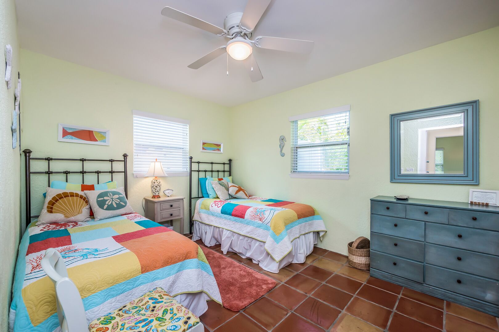 A bedroom with two beds, a ceiling fan, a dresser, and a window with blinds.