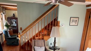 A living room with a wooden floor, a staircase, a ceiling fan, and a green armchair.