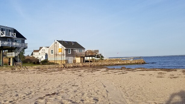 A beach with houses, a stone wall, and a clear sky.