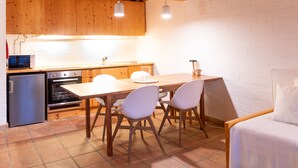 Eine kleine Küche mit Holzausstattung, ein Essbereich mit Tisch und Stühlen sowie ein Bett mit weißer Bettwäsche.