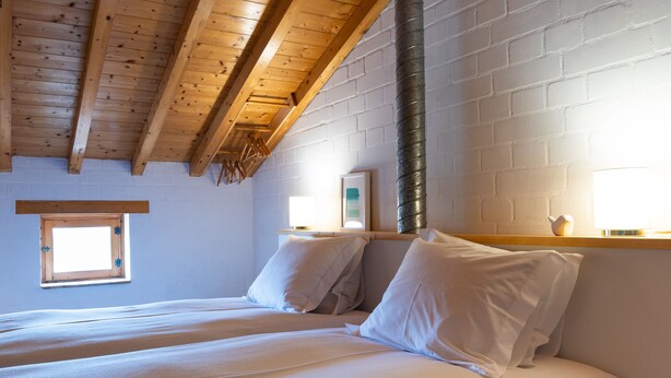 Ein Schlafzimmer mit zwei Betten, Holzbalken an der Decke, einer Backsteinwand und einem kleinen Fenster.