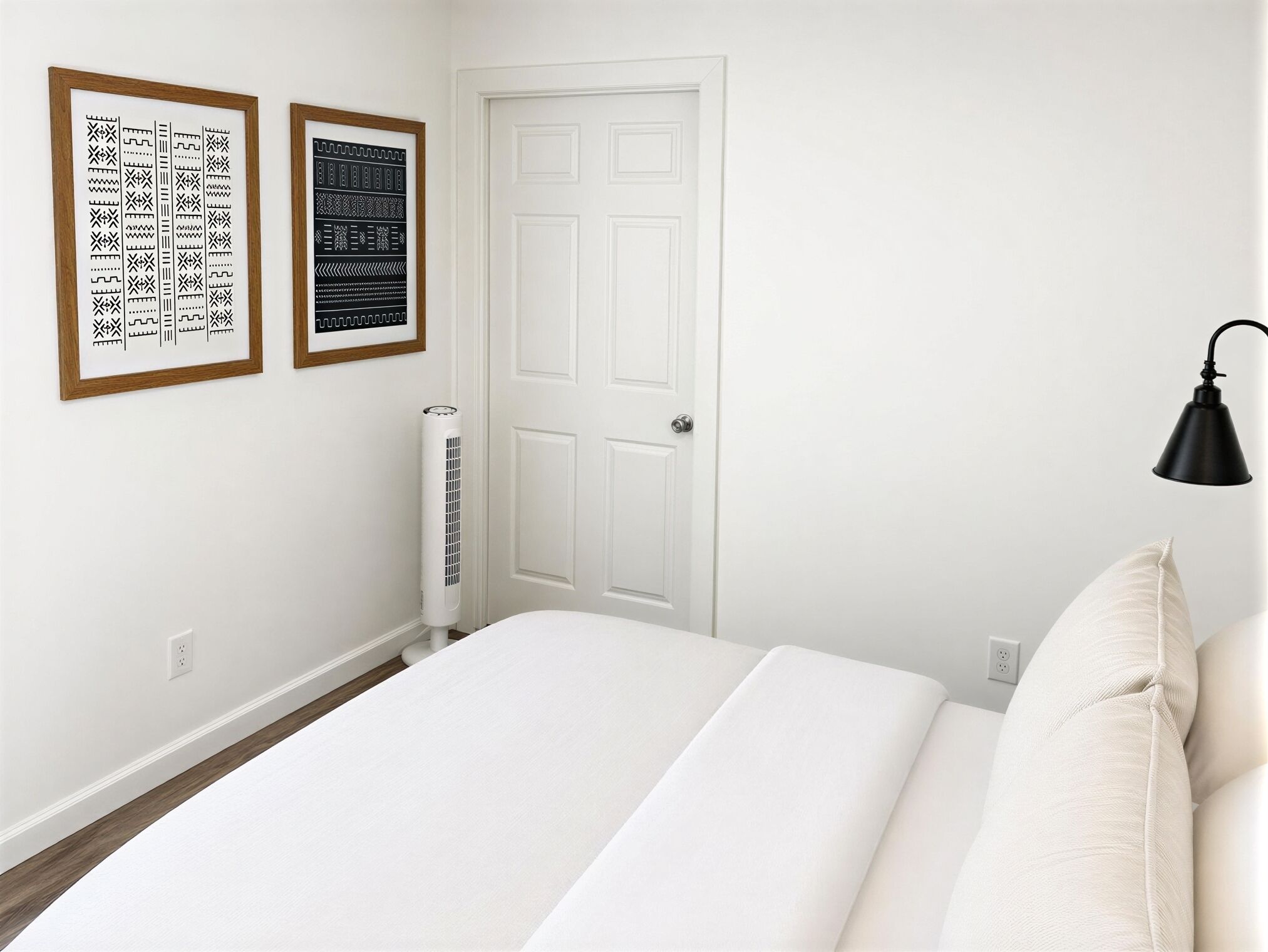 A bedroom with a bed, a white door, a wall-mounted heater, and two framed pictures.