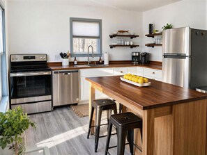 Une cuisine moderne dotée d’un four encastré, d’un lave-vaisselle, d’un réfrigérateur en acier inoxydable, de plans de travail en bois et de tabourets de bar.