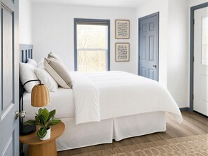 Une chambre à coucher avec un lit, une table de chevet avec une lampe, une plante et deux tableaux encadrés accrochés au mur.