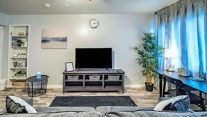 Un salon moderne avec un canapé gris, un téléviseur à écran plat, une petite table d’appoint et une bibliothèque.
