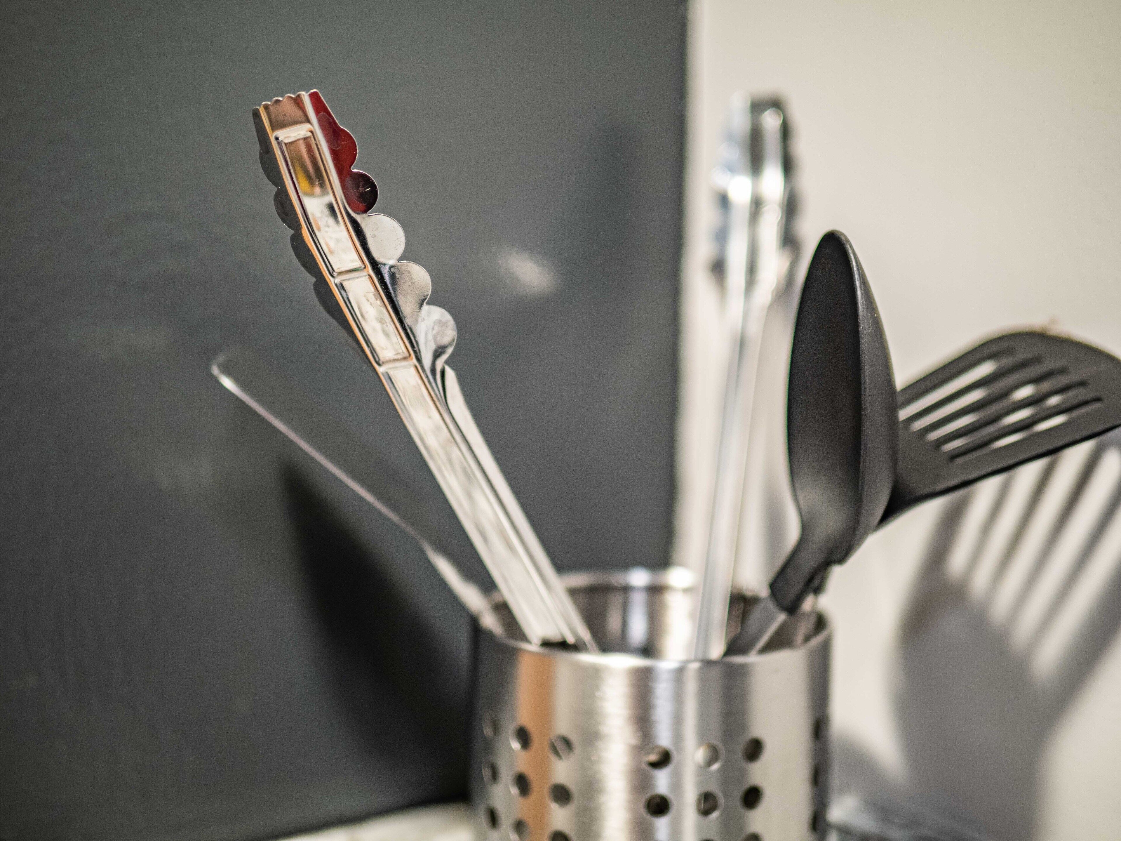 A kitchen utensil holder with a metal spoon, spatula, and a red-handled utensil.