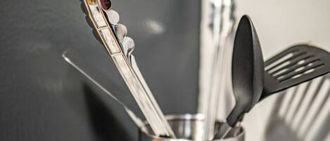 A kitchen utensil holder with a metal spoon, spatula, and a red-handled utensil.