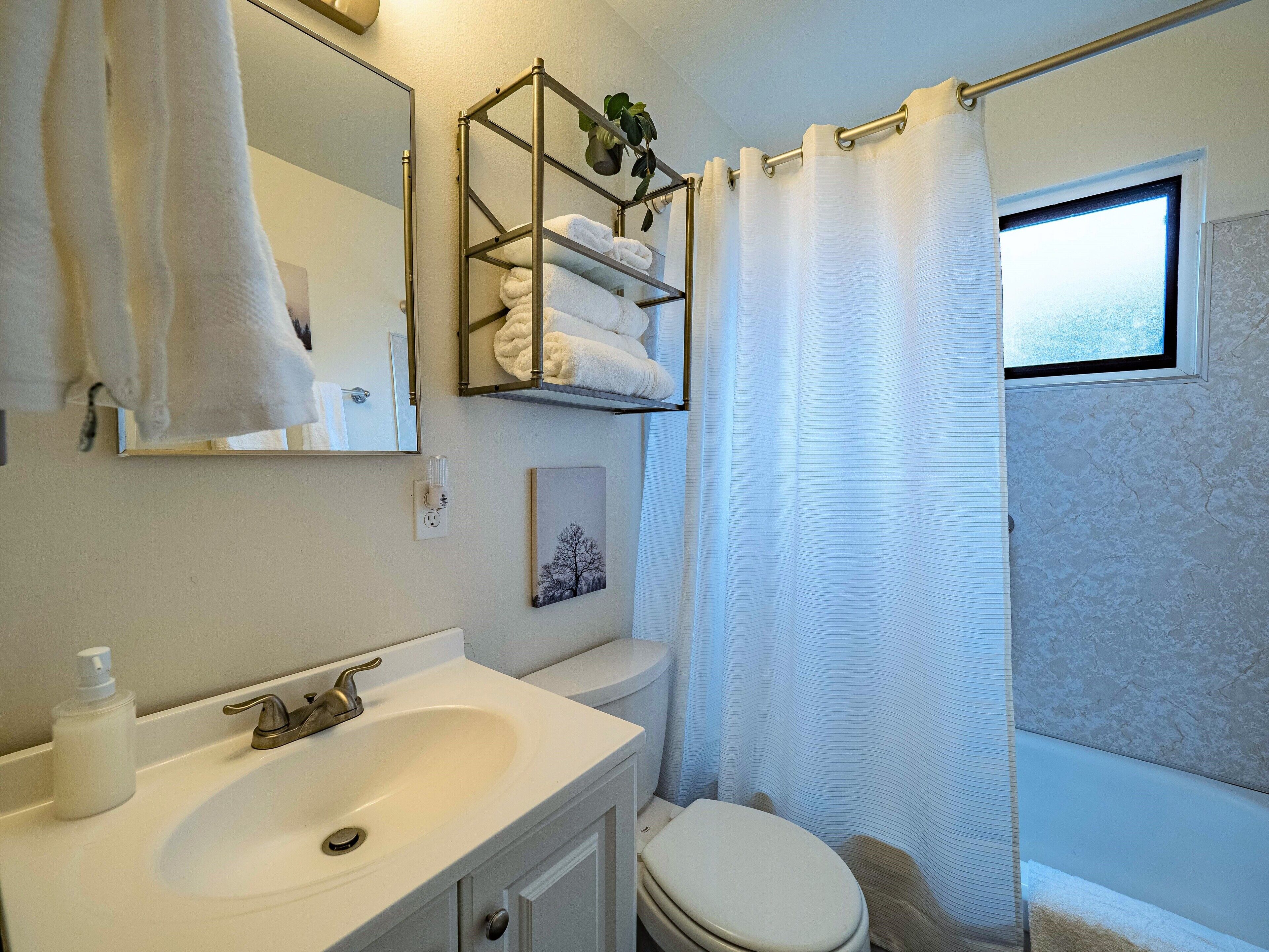 Une salle de bain avec un lavabo blanc, des toilettes, un porte-serviettes avec des serviettes pliées, un tableau encadré au mur et un rideau de douche.
