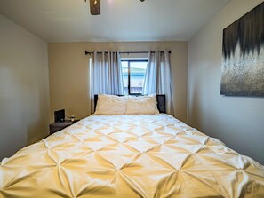 A bedroom with a bed, curtains, a painting, and a window.