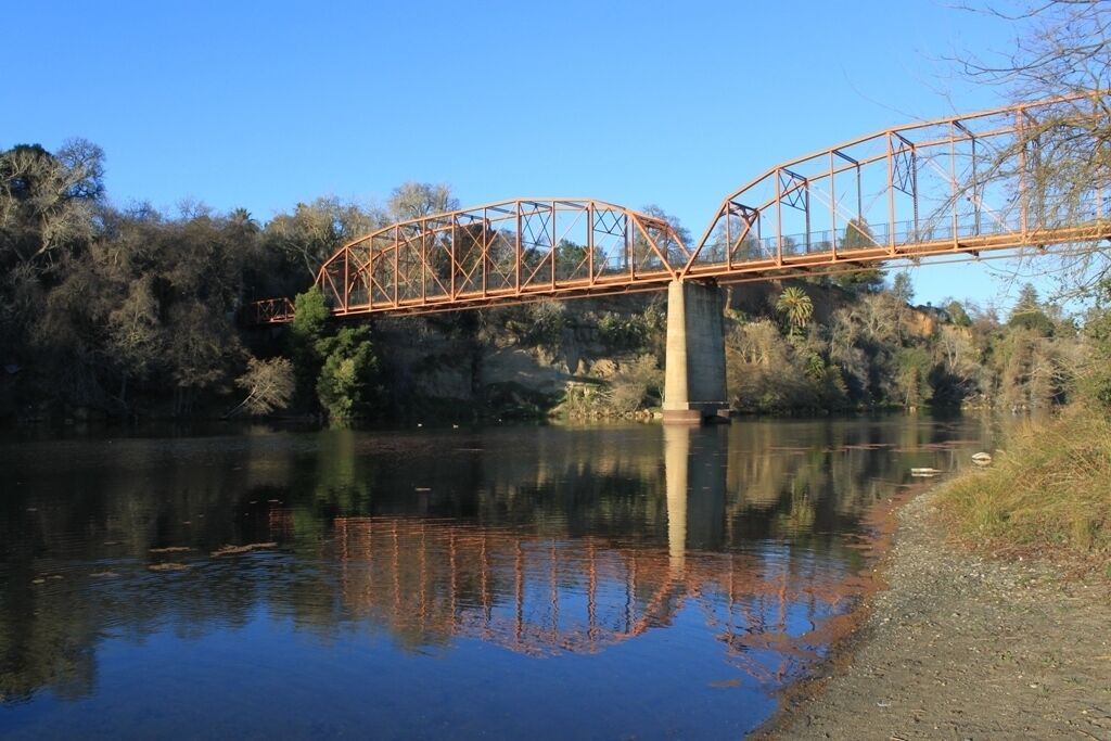 A metal bridge over a calm river with trees in the background.