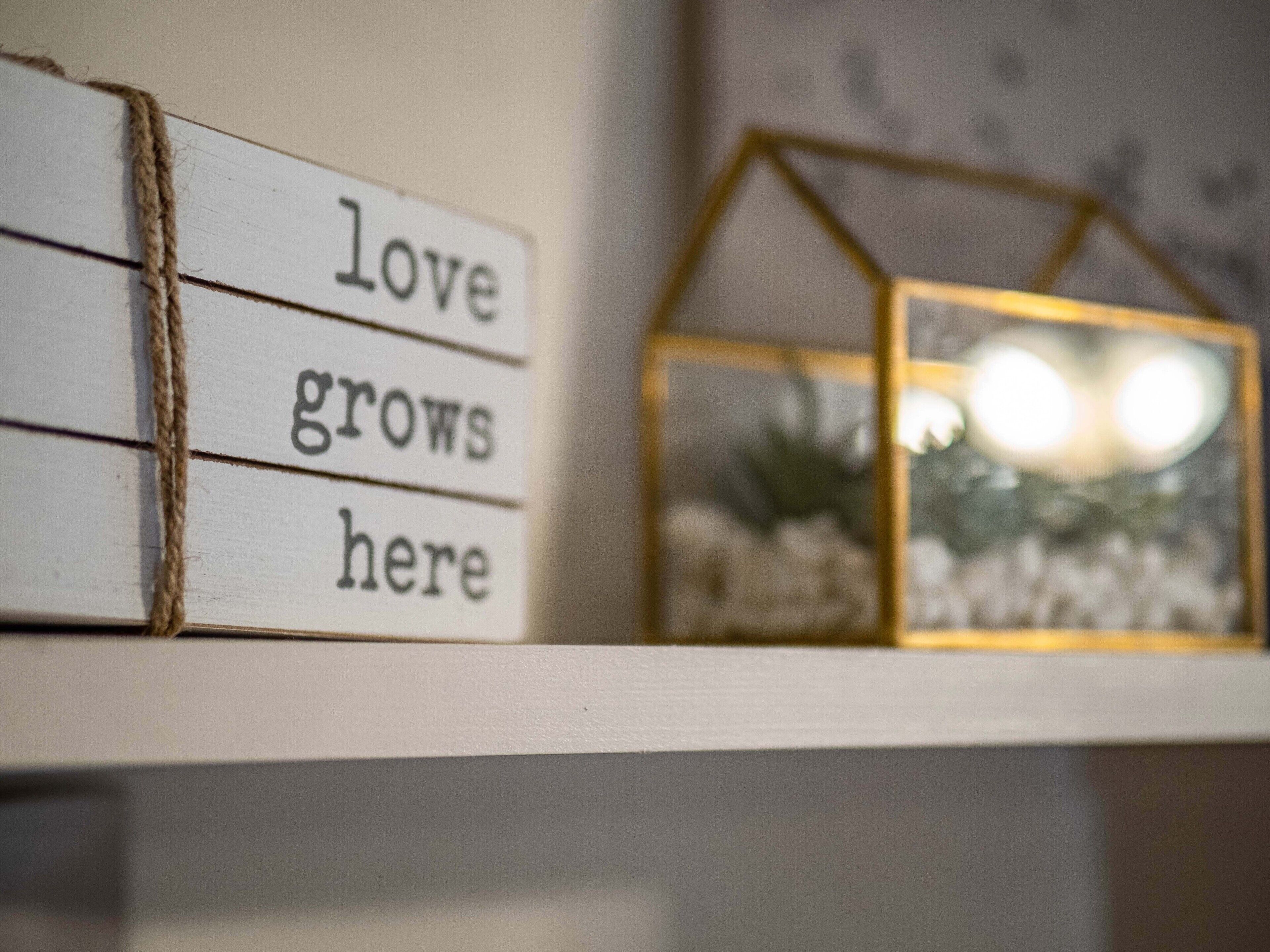 Una estantería con un cartel que dice “el amor florece aquí” y una pequeña decoración con forma de casa.