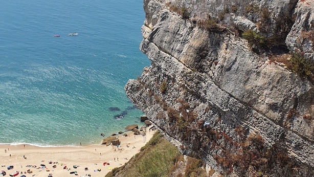 Un acantilado costero con una playa en la base, una estructura de piedra en el acantilado y un farol.