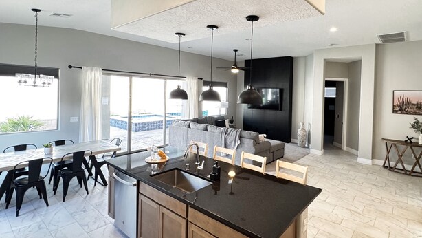 A modern kitchen with a central island, dining area with chairs, and a large window offering a view. - Chill. Grill. Putt. Splash. Play. Your Private Pool Paradise Awaits! (Mesquite)