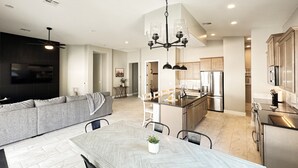A modern kitchen with a central island, stainless steel appliances, and a dining area with a herringbone-patterned table. - Chill. Grill. Putt. Splash. Play. Your Private Pool Paradise Awaits! (Mesquite)
