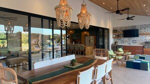 A modern dining area with a wooden table, wicker chairs, and hanging crystal chandeliers. - Casa Palmeras • Luxury Villa Near Beach & Surf (Tamarindo)