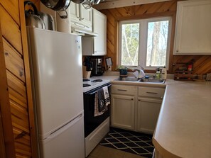 Una cocina con armarios de madera, un refrigerador blanco, una estufa, un lavamanos y una ventana con vista a árboles.