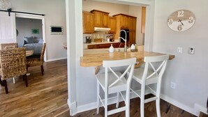 A modern kitchen with wooden cabinets, a central island with chairs, and a 'HOME' sign above the island. - Serenity Waterfront 4BR w/ Private Dock, Heated Pool & Relaxing Hot Tub (Palm Coast)