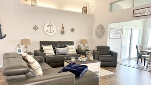 A modern living room with a sectional sofa, a coffee table, and decorative wall art. - Serenity Waterfront 4BR w/ Private Dock, Heated Pool & Relaxing Hot Tub (Palm Coast)