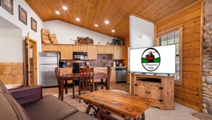 A cozy cabin-style kitchen with wooden cabinets, a dining area with a wooden table and chairs, and a stone wall on one side. - Romantic Studio Cabin for Two with Private Balcony, Jetted Tub, and Gas Fireplace (Branson)