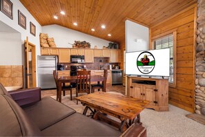 Une cuisine chaleureuse, aménagée dans le style d’un chalet, avec des meubles en bois, un coin repas doté d’une table et de chaises en bois, et un mur en pierre sur l’un des côtés.