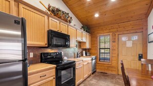 A kitchen with wooden cabinets, a stainless steel refrigerator, a microwave, an oven, and a dishwasher. - Romantic Studio Cabin for Two with Private Balcony, Jetted Tub, and Gas Fireplace (Branson)