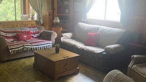 A cozy living room with a wooden floor, a sofa, a chair, and a small table. - Tranquil 3 bedroom waterfront cottage on private lake! (Rideau Lakes)