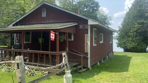 A rustic wooden building with a porch, a Canadian flag, and a welcome sign. - Tranquil 3 bedroom waterfront cottage on private lake! (Rideau Lakes)