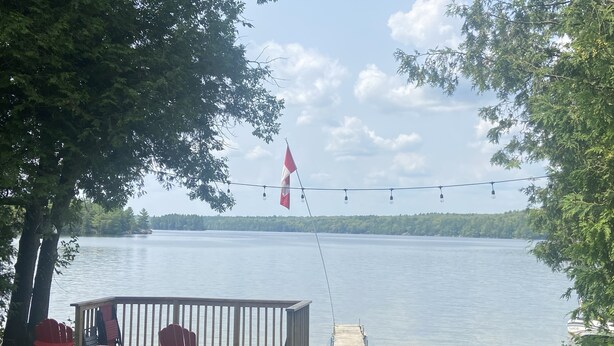 A wooden deck with red Adirondack chairs, a small table, and a flag. - Tranquil 3 bedroom waterfront cottage on private lake! (Rideau Lakes)