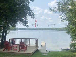 A wooden deck with red Adirondack chairs, a small table, and a flag. - Tranquil 3 bedroom waterfront cottage on private lake! (Rideau Lakes)