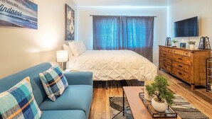 Un dormitorio moderno con cama, sofá azul, cómoda de madera y televisor.