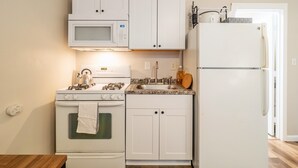 Una cocina compacta con gabinetes blancos, microondas, estufa, pileta y refrigerador.