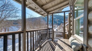 A wooden deck with a bench and pillows, overlooking a snowy landscape and a clear sky.
