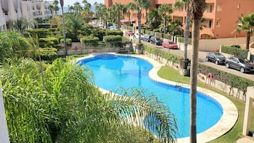 Una piscina rodeada de palmeras y vegetación, con vista a un área residencial al fondo.