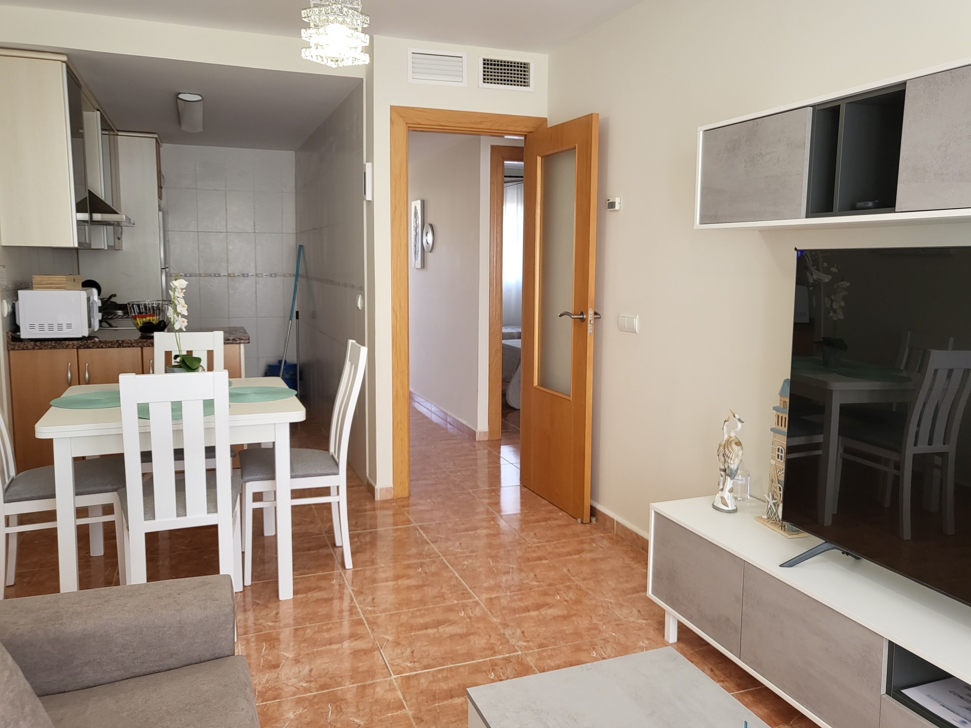 Una cocina moderna con armarios blancos, un microondas y un comedor con mesa y sillas blancas.