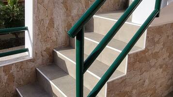 Una escalera con paredes de piedra y barandillas de metal verde.