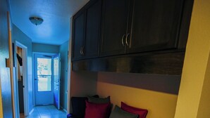Een hal met een donkergrijze bank tegen een muur, een deur en een plafondlamp.