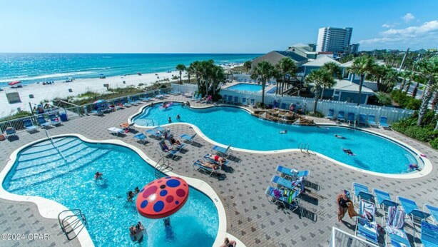 Uma área de piscina com várias piscinas, espreguiçadeiras e vista para a praia.