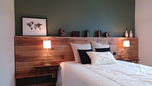 Un dormitorio con cabecera de madera, un mapa mundial enmarcado y la palabra 'SMILE' en la pared. Hay dos mesitas de noche con lámparas.
