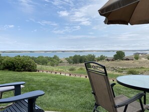 Eine Terrasse mit Seeblick, umgeben von viel Grün und einigen Gebäuden in der Ferne.