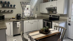 Une cuisine avec des meubles blancs, un plan de travail en granit, un ventilateur de plafond et un coin repas comprenant une table et des chaises.
