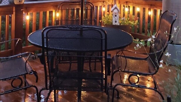 Une terrasse extérieure avec une table ronde et des chaises, un grand parasol et un éclairage décoratif.