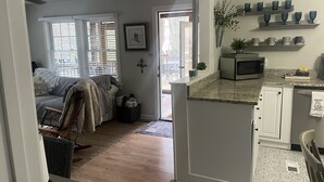 Un intérieur de maison comprenant une cuisine, un coin repas et un salon. On y trouve un four à micro-ondes, un évier et une fenêtre avec des stores.