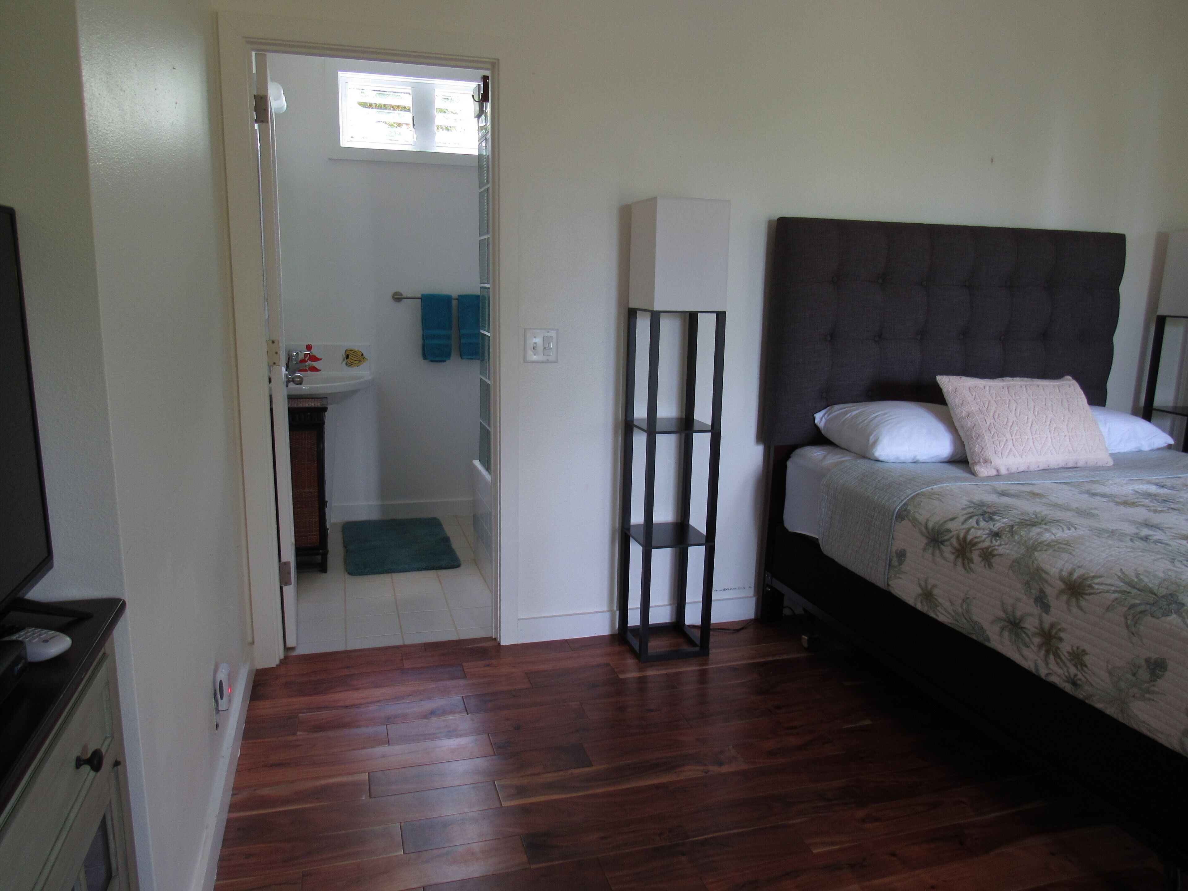A bedroom with a wooden floor, a bed with a floral bedspread, a bedside table, and a nightstand.