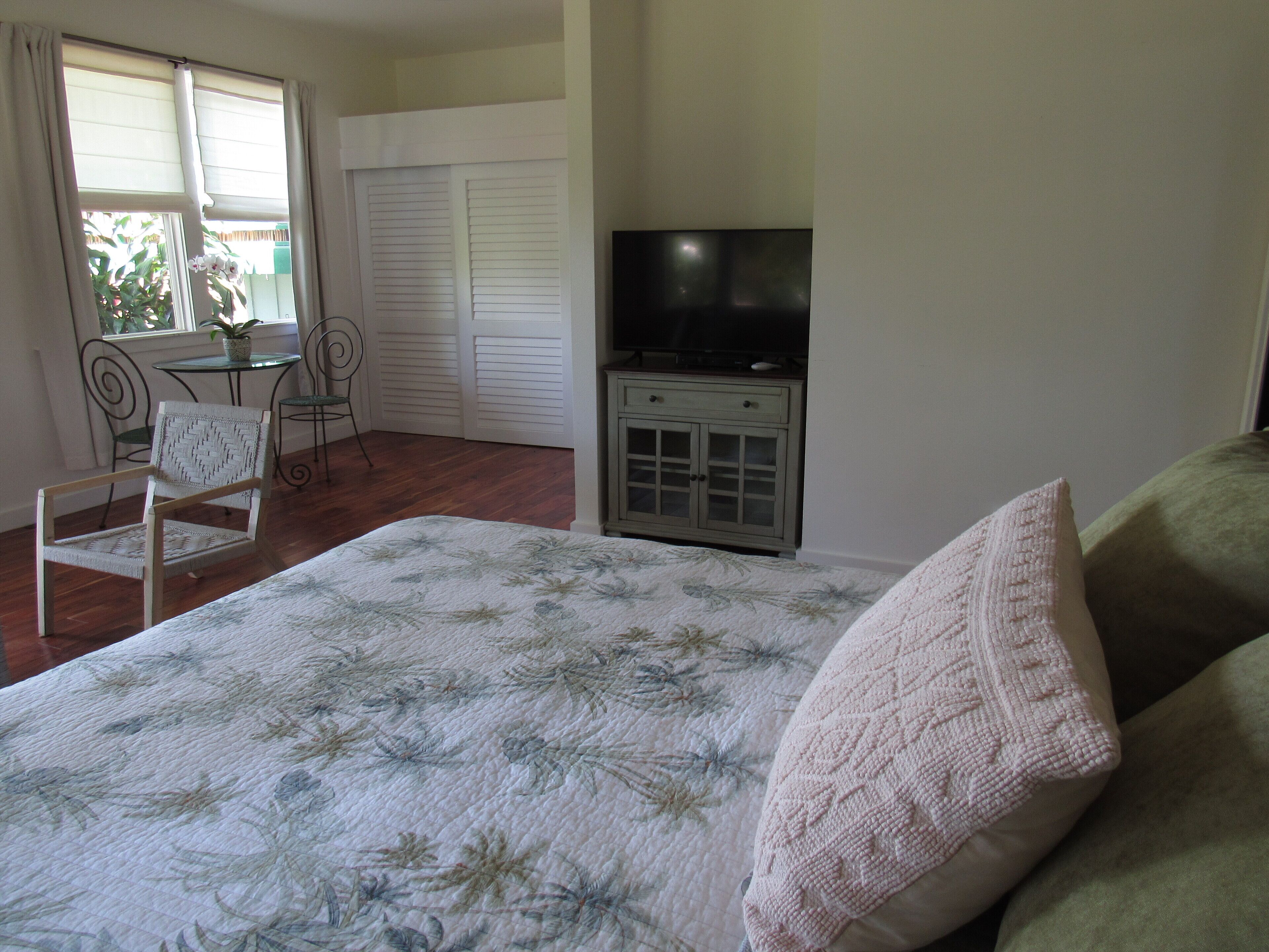 A bedroom with a bed, a TV, a desk with a chair, and a window with curtains.