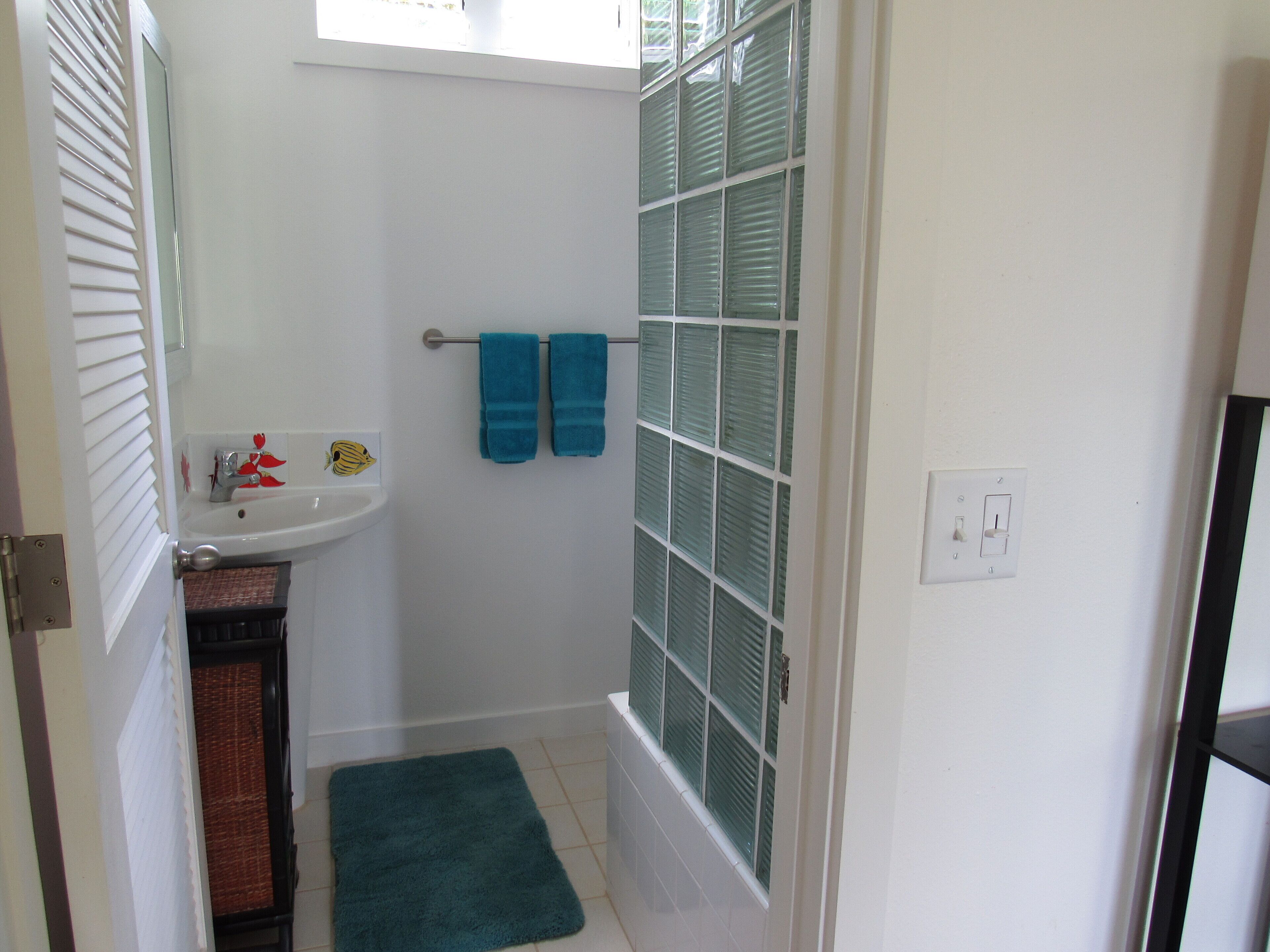 Une salle de bain avec un lavabo blanc, un miroir, un porte-serviettes avec deux serviettes, une douche avec des portes en verre et un tapis de bain vert.