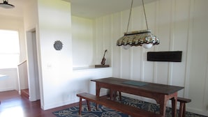 Ein Essbereich mit einem Holztisch und Bänken, einem gemusterten Teppich, einer hängenden Leuchte und einem an der Wand befestigten Schild.