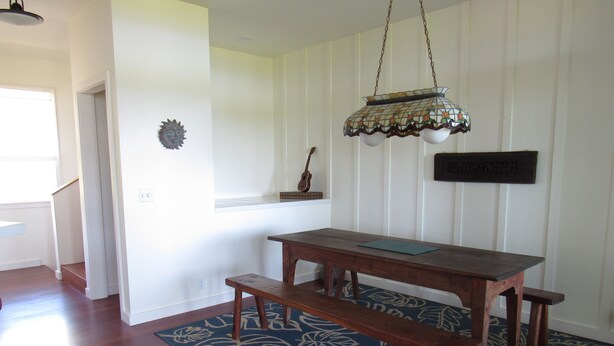 Een eetgedeelte met een houten tafel en banken, een kamerkleed met een patroon, een hanglamp en een aan de muur bevestigd bord.