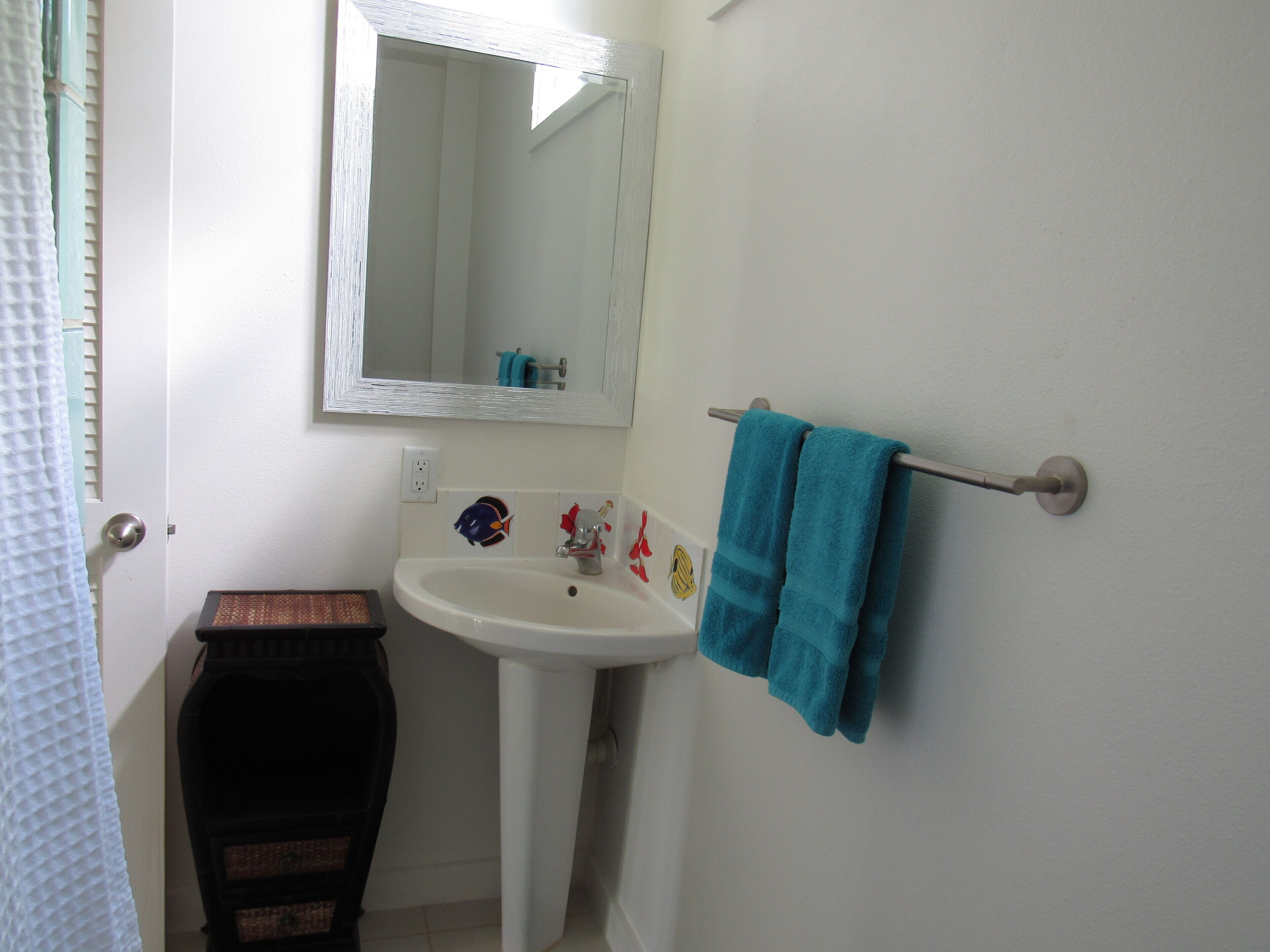 Une salle de bain avec un lavabo blanc, un miroir et un porte-serviettes sur lequel est posée une serviette bleue.