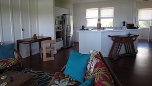 Eine moderne Küche mit Einbauofen und Kühlschrank, ein Essbereich mit Holztisch und Stühlen sowie ein Wohnbereich mit Sofa und Couchtisch.