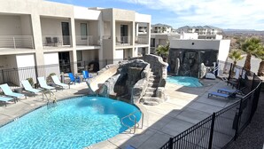 Un espace piscine comprenant deux piscines, des chaises longues et une cascade artificielle en roches.